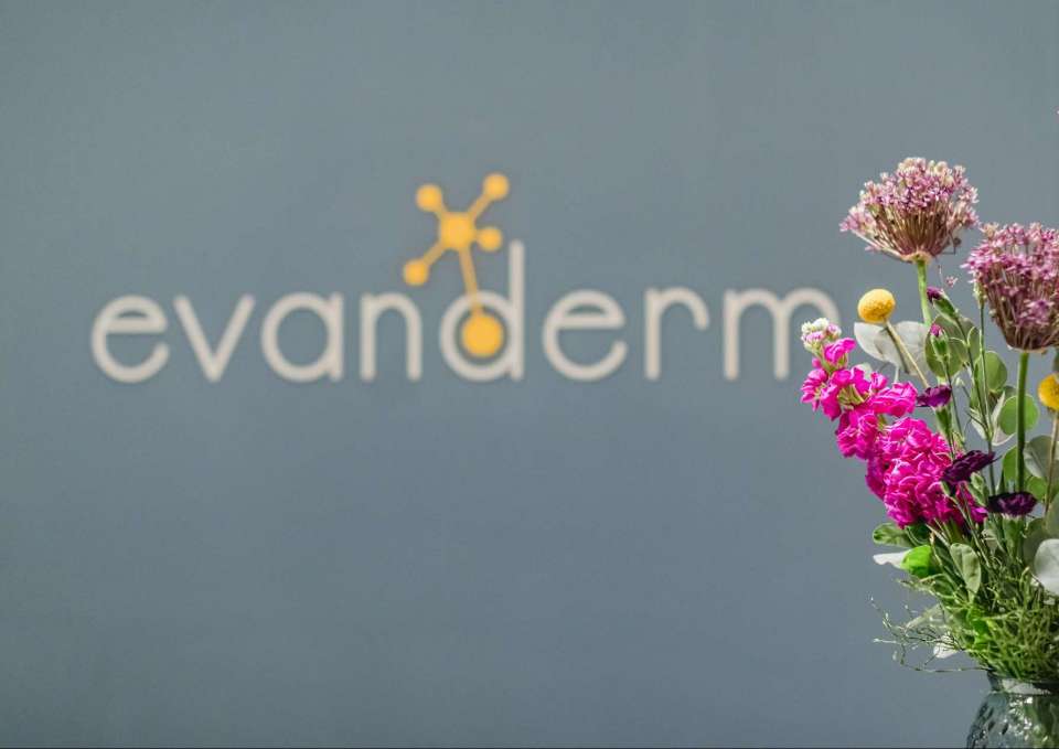 Das Bild zeigt das Logo evanderm sowie einen Blumenstrauß im Empfangsbereich der Praxis.